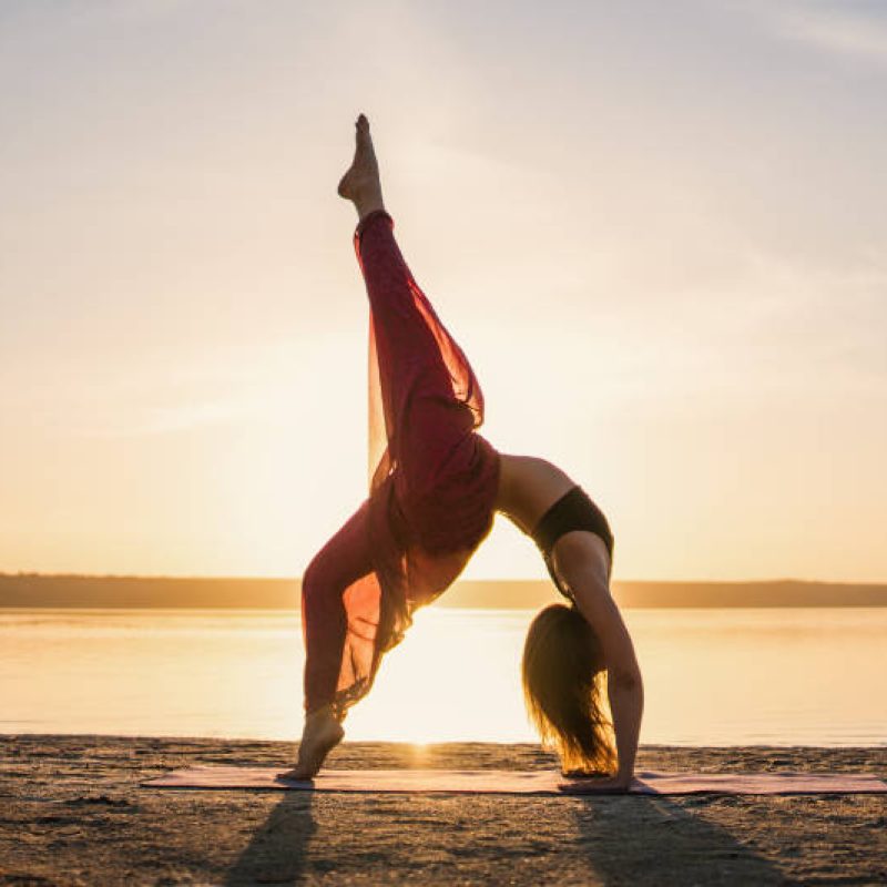 Silhouette woman on the beach at sunset doing yoga asana. Morning natural stretch warm-up training